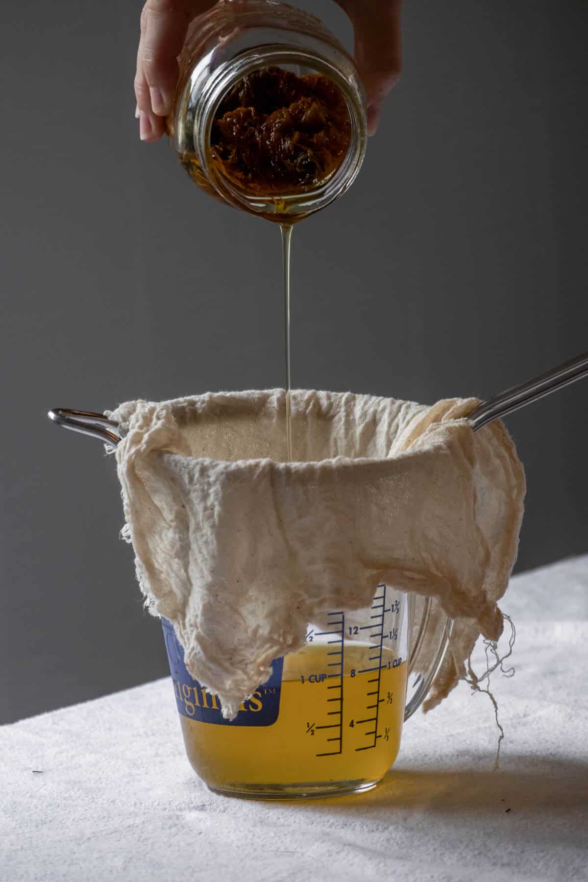 Infused calendula oil being strained through a cheesecloth