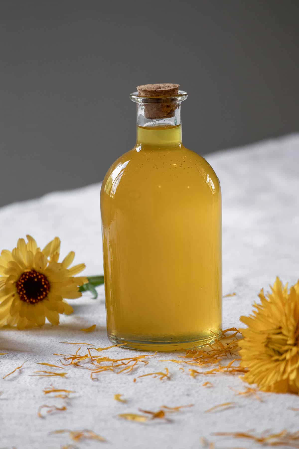 A bottle of calendula oil next to calendula flowers