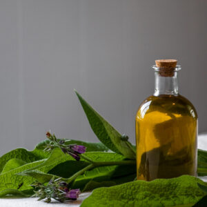 A bottle of comfrey oil next to comfrey leaves