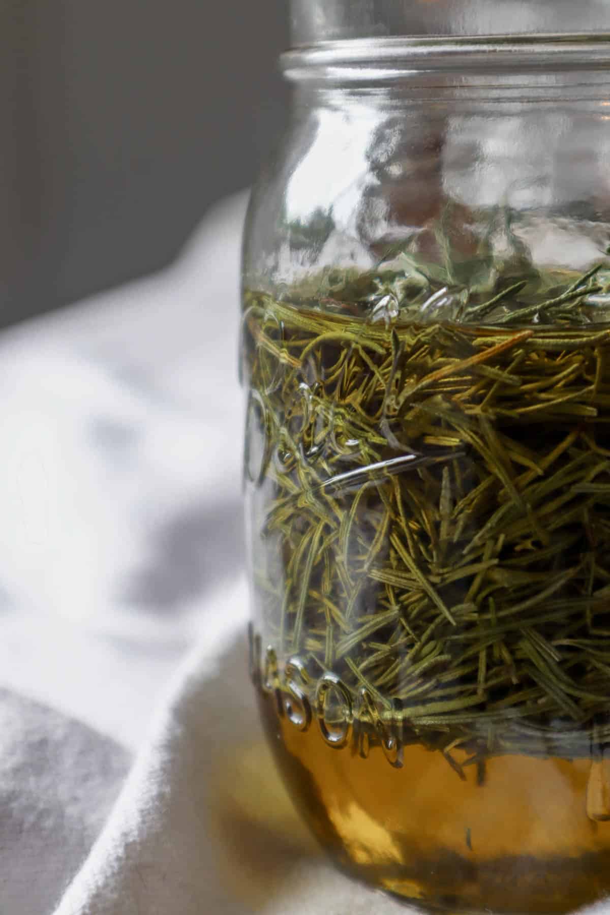 Ball jar of dried rosemary leaves infusing in oil