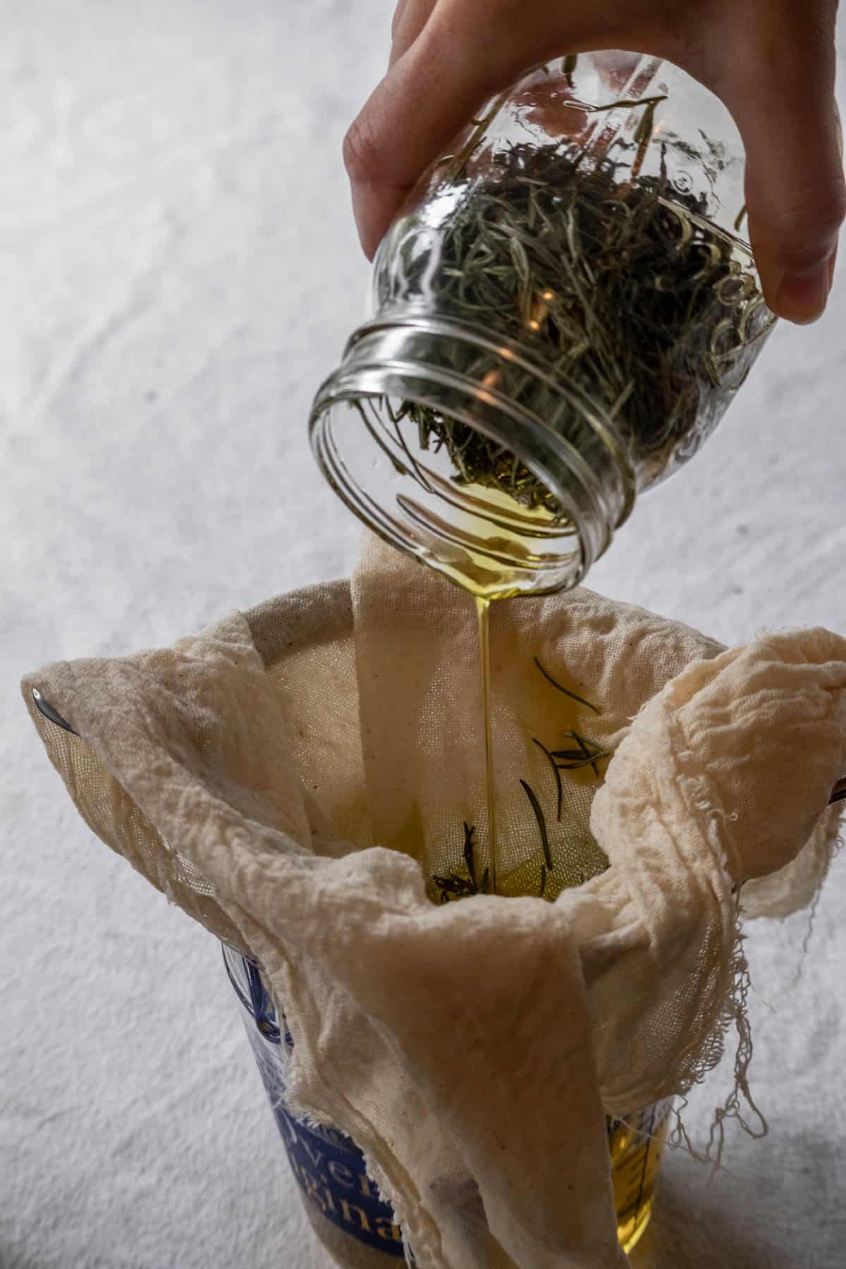 Rosemary oil being poured through a cheesecloth