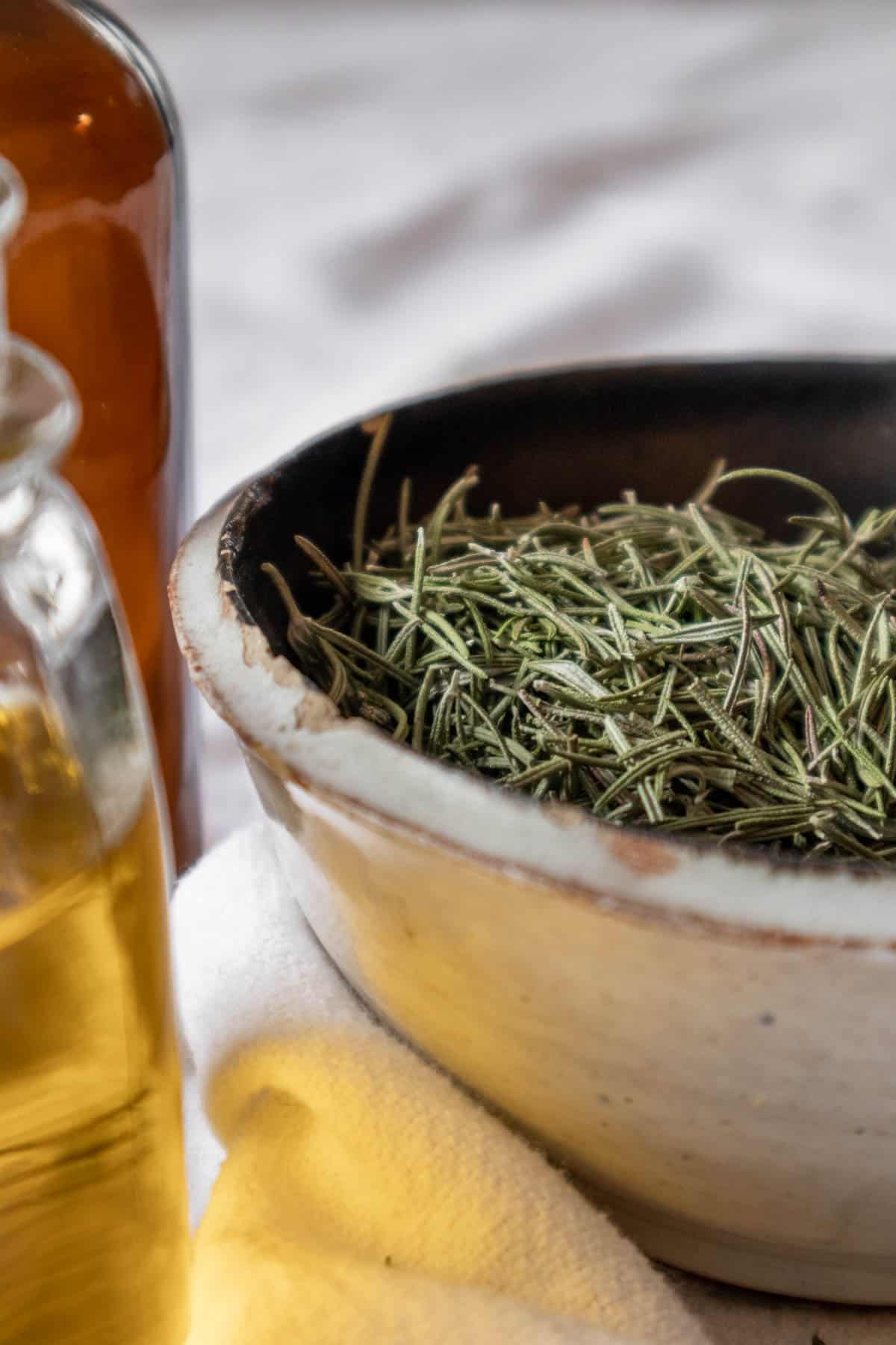 Bowl of dried rosemary leaves next to a jar of oil