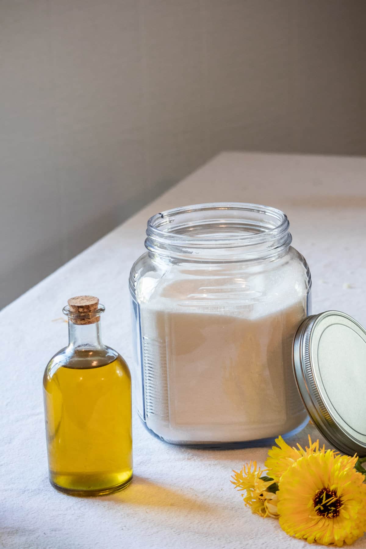A bottle of calendula oil next to a container of sugar