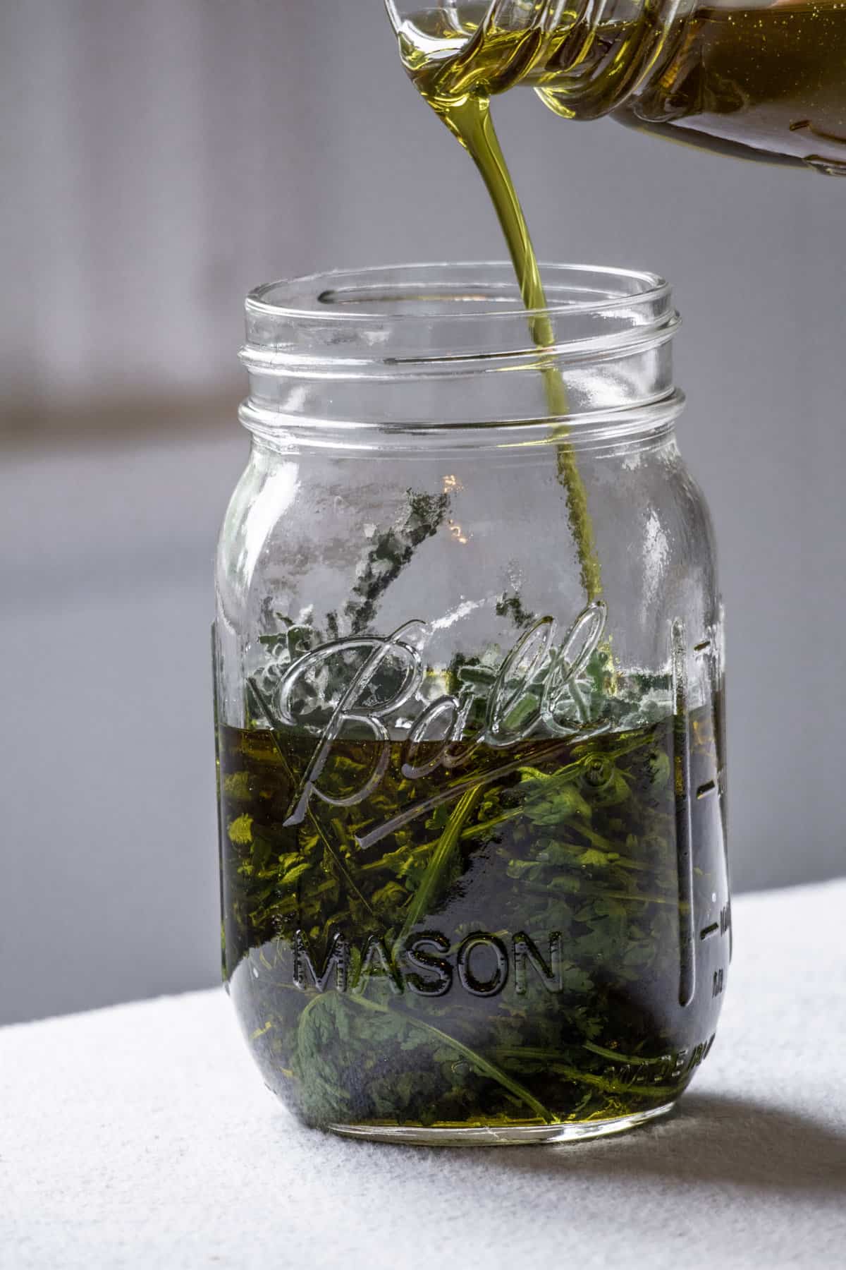 Olive oil being poured into a jar of yarrow leaves