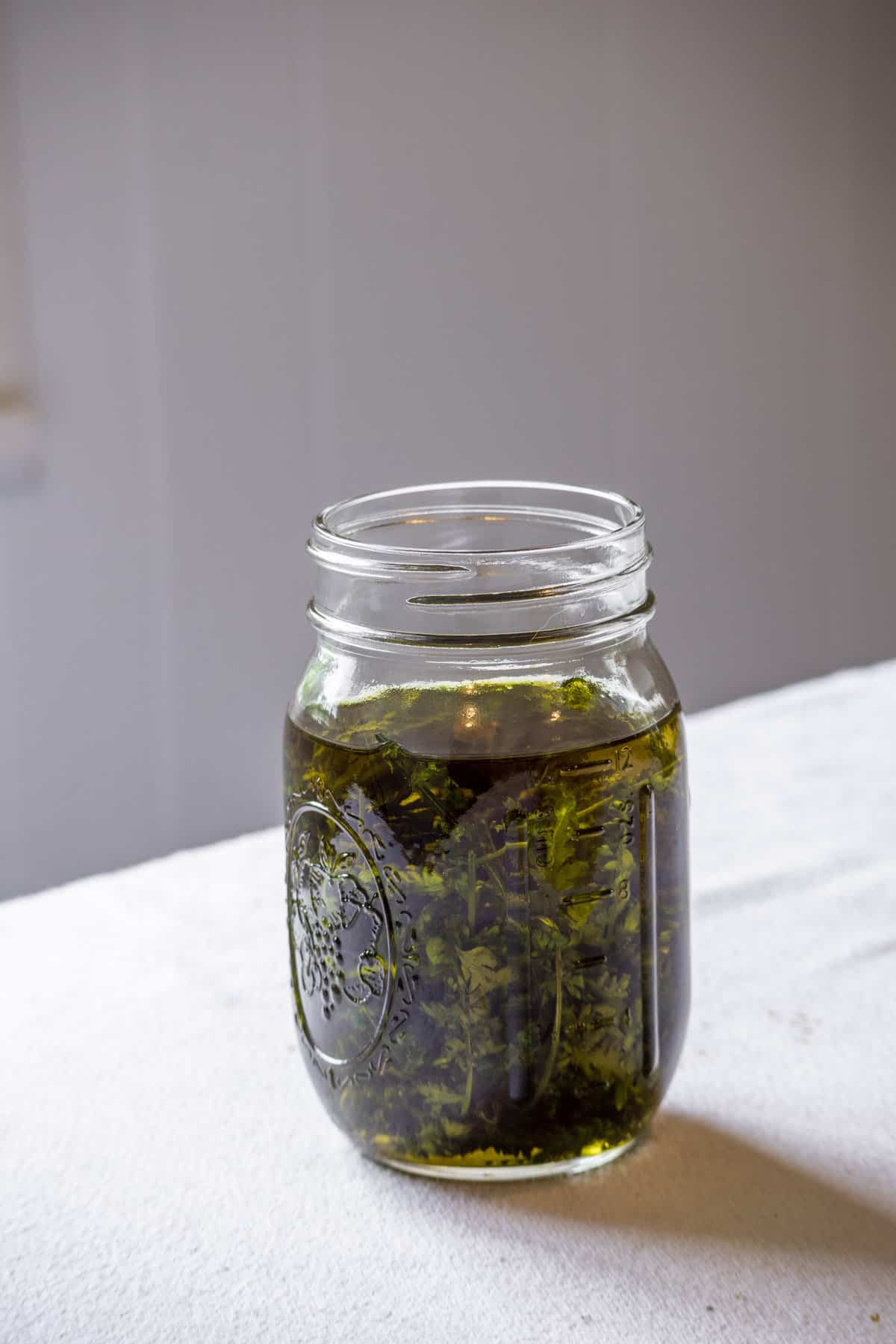 A jar of yarrow infused oil on a white table